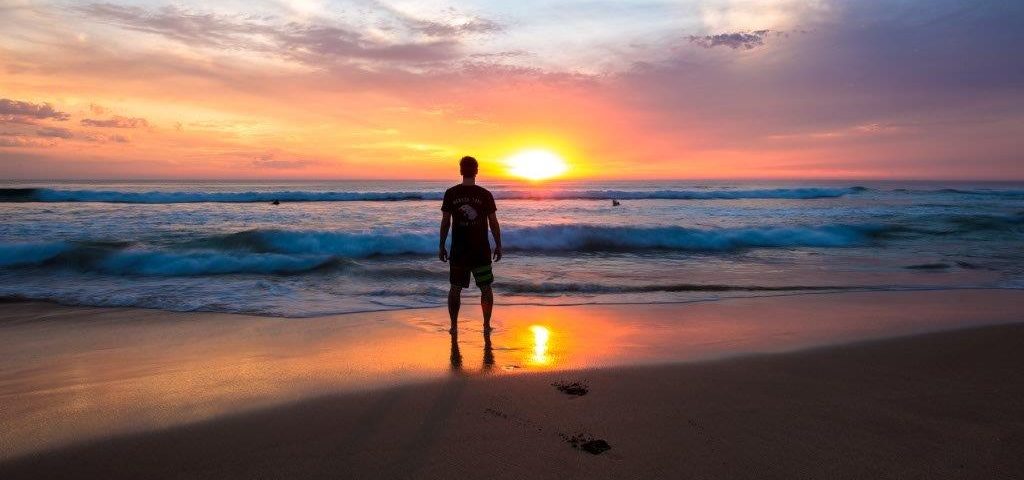 Ein Mann steht bei Sonnenuntergang am Strand.