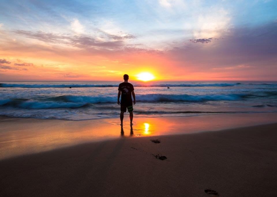 Ein Mann steht bei Sonnenuntergang am Strand.